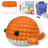 An orange crochet whale amigurumi toy with a gray belly, shown next to yarn and craft accessories.