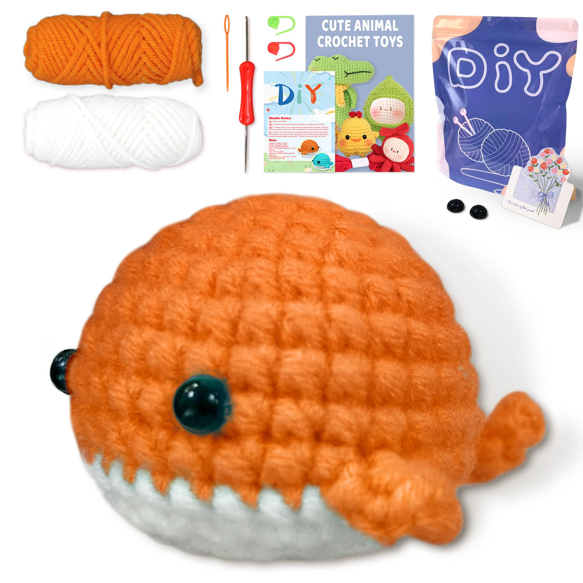 An orange crochet whale amigurumi toy with a gray belly, shown next to yarn and craft accessories.