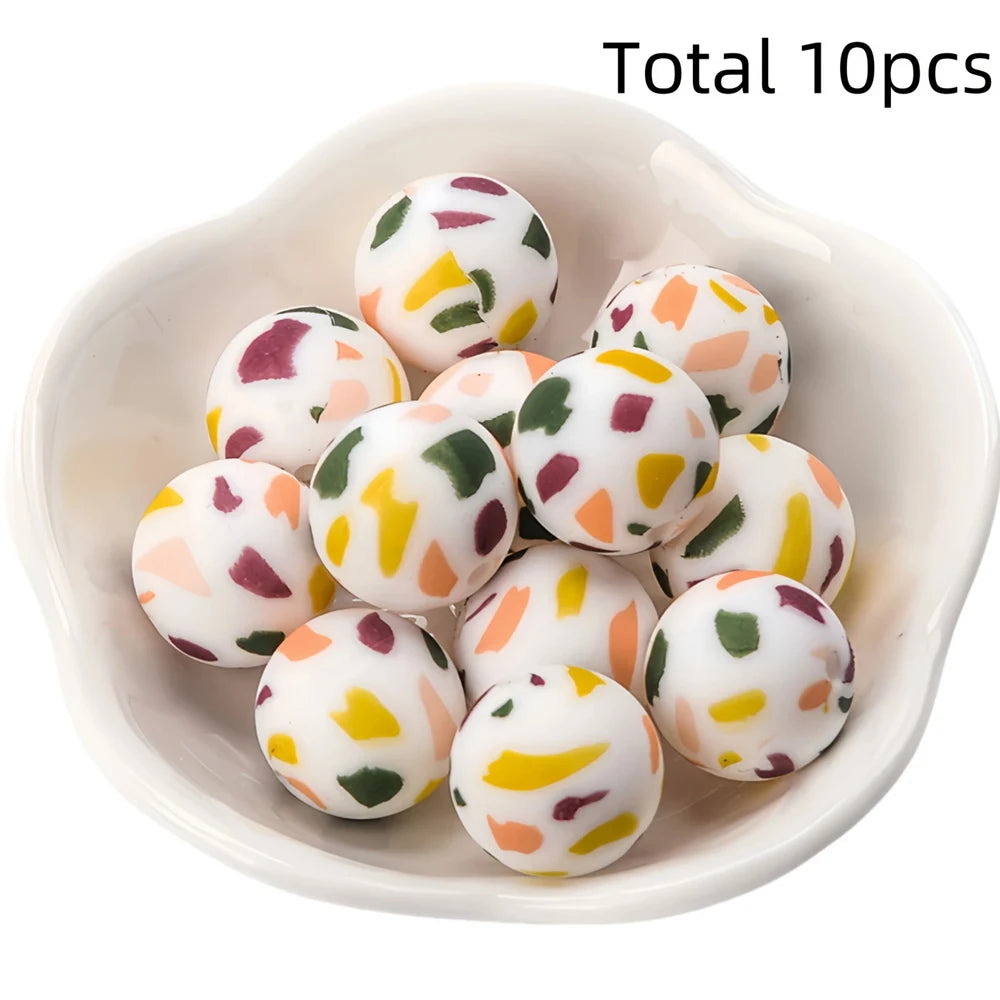 A bowl filled with ten white silicone beads printed with colorful floral patterns for DIY jewelry making