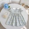 A light blue floral bubble sleeve dress for girls displayed on a white table with pearls and a wooden cup.