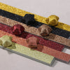 A collection of glitter origami star paper strips in various colors like gold, black, silver, and rose gold arranged diagonal