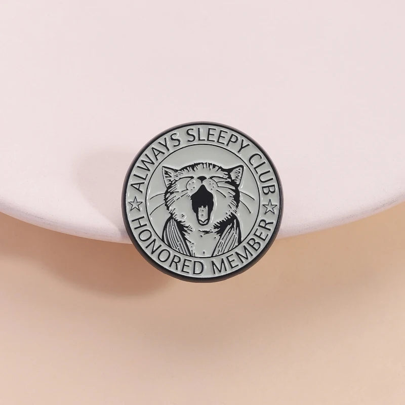 An enamel pin featuring a stylized yawning cat design and the text Always Sleepy Club Honored Member