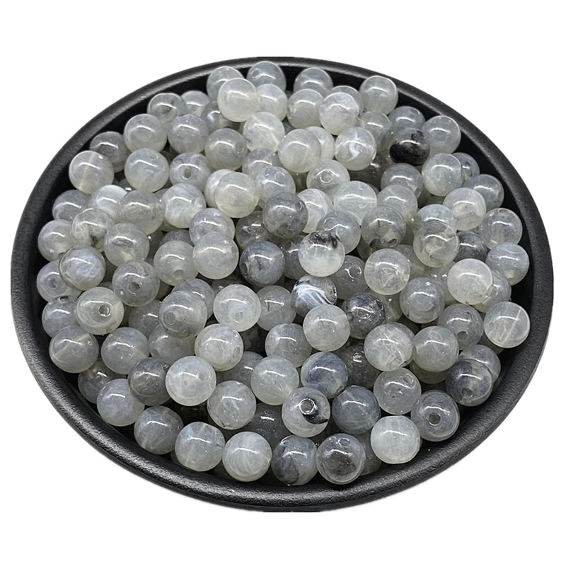 A pile of clear and gray acrylic round beads for jewelry making in a black bowl.