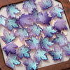 Purple and blue iridescent maple leaf glass beads arranged on a light background.