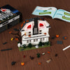 A set of haunted horror house building blocks featuring a white house model and movie-inspired accessories on a wooden surfac