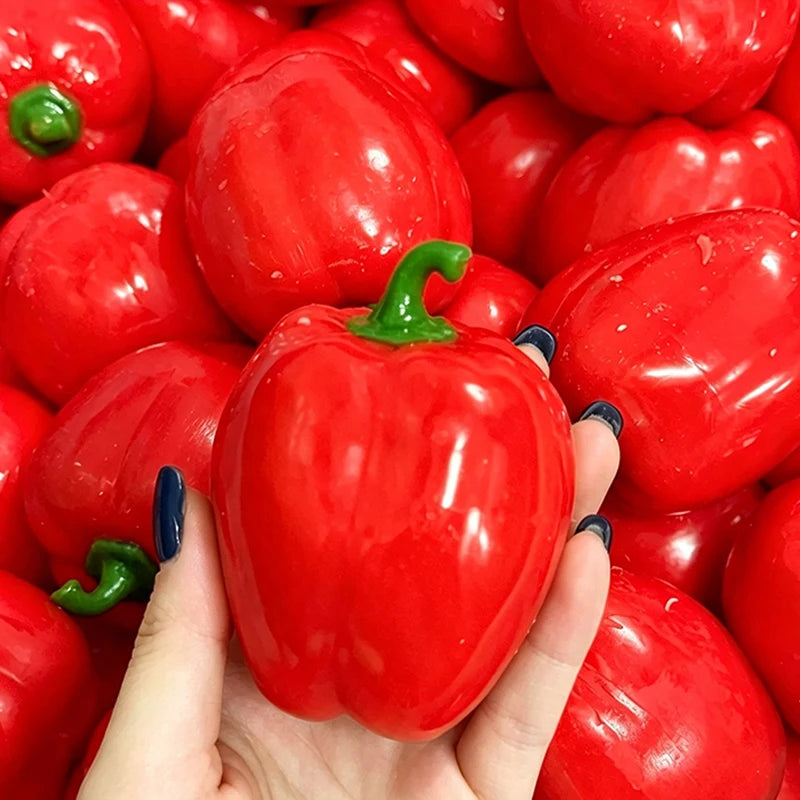 A hand holds a bright red bell pepper, showing its glossy texture and vibrant color.