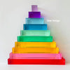 A tower of rainbow acrylic building blocks in various shades of purple, blue, green, yellow, and pink.