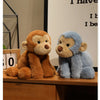 Two plush monkey soft toys, one brown and one blue, sitting on a wooden surface.