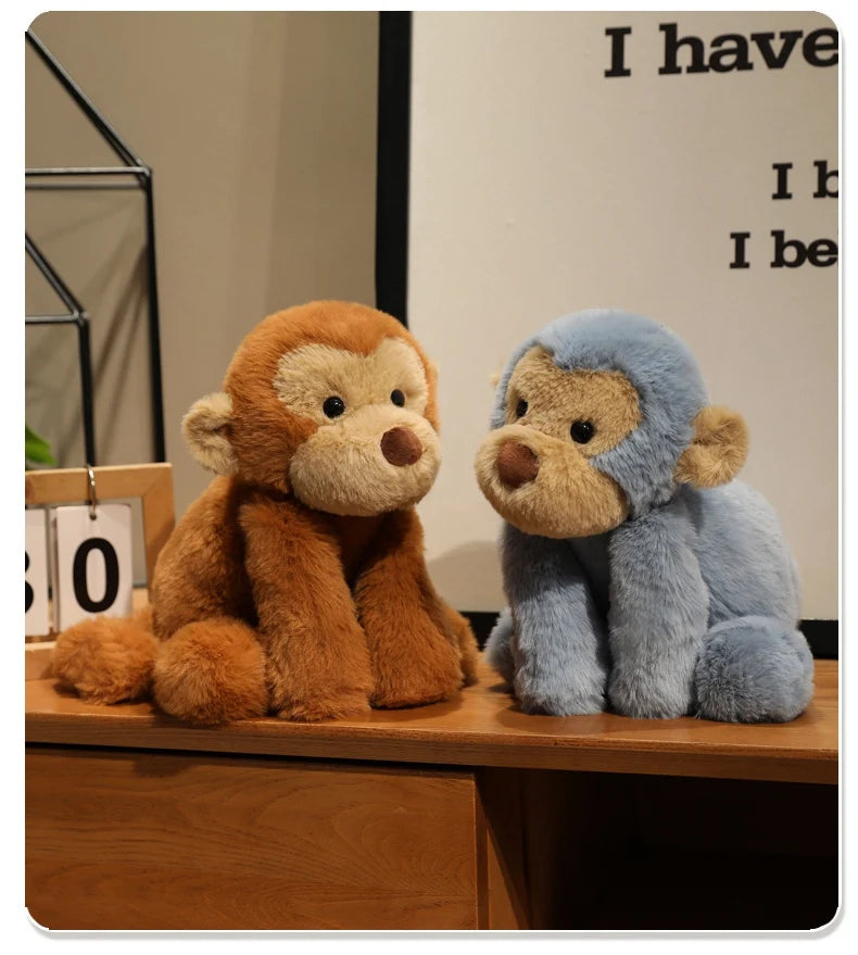 Two plush monkey soft toys, one brown and one blue, sitting on a wooden surface.