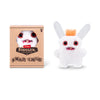 A plush toy of a white monster with large red eyes and orange tufts, packaged in a box.