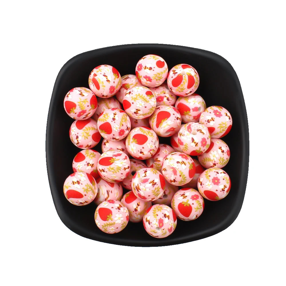 A black bowl filled with pink and yellow printed silicone beads for jewelry making.