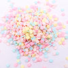 A pile of colorful polymer clay flower charms in pink, yellow, and blue scattered on a white surface.