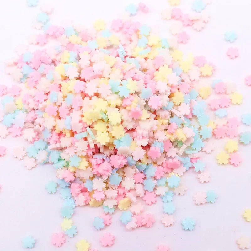 A pile of colorful polymer clay flower charms in pink, yellow, and blue scattered on a white surface.