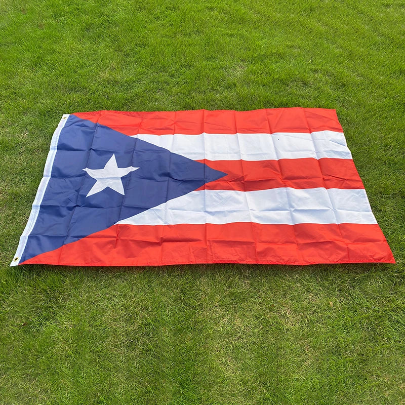A large, rectangular flag of Puerto Rico with red and white stripes and a blue triangle featuring a white star, laid out on g