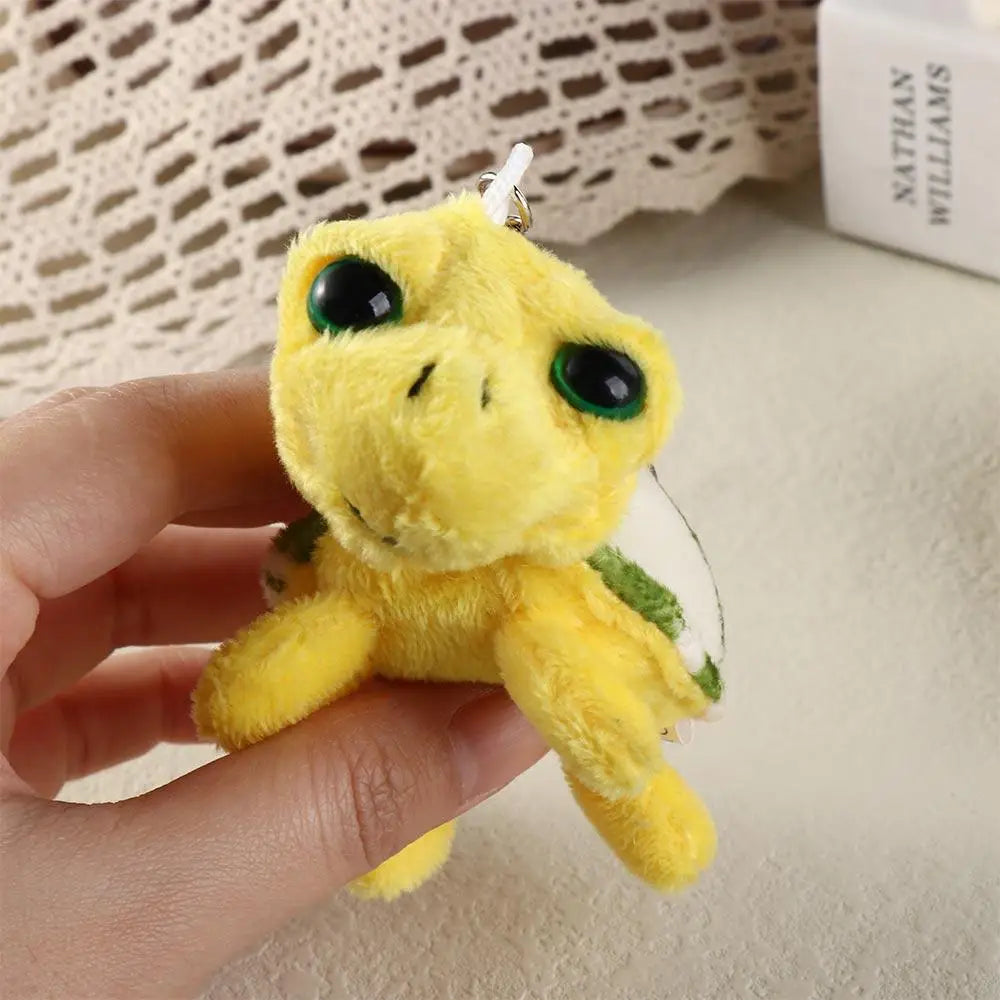 A yellow turtle plush toy with green accents is being held, featuring a keyring attachment.
