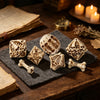 A set of carved bone skull polyhedral dice resting on a dark fabric next to old books and candles.
