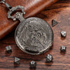 A silver steampunk dragon pocket watch dice case with seven small dice resting on a dark wooden surface.