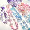 A collection of mixed acrylic bow and flower beads in various shades of purple, pink, blue, and clear for jewelry making.