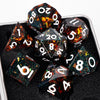 A collection of black resin dice with sharp edges and colorful internal glitter set against a dark surface.