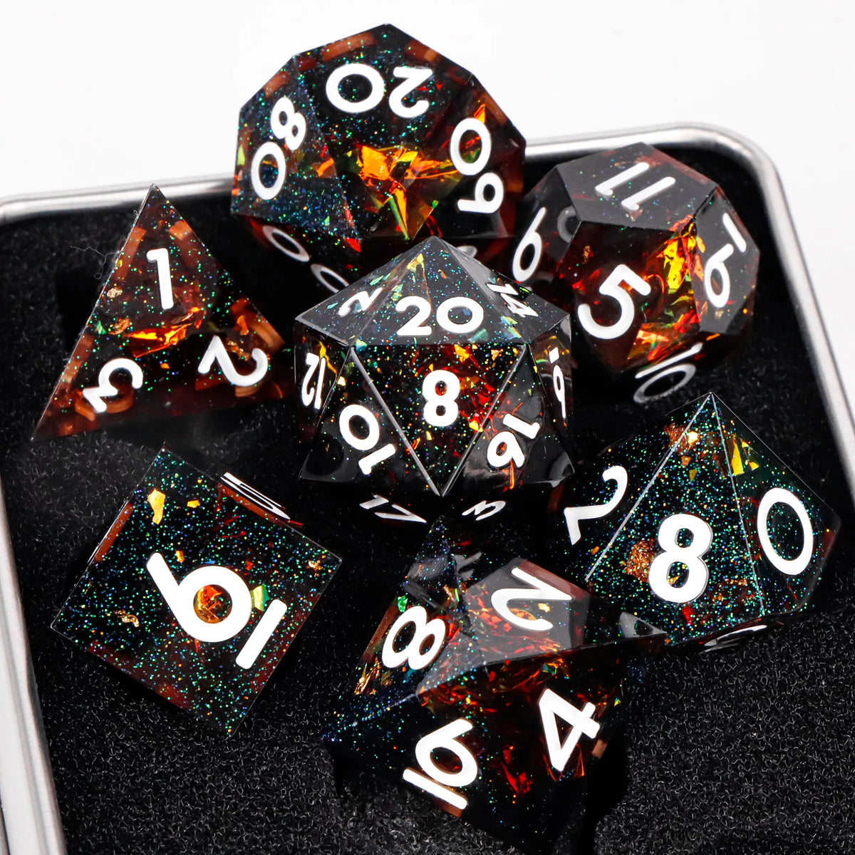 A collection of black resin dice with sharp edges and colorful internal glitter set against a dark surface.