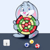 A cartoon gray rabbit holding a dartboard with colored targets and several small balls on a dark surface.