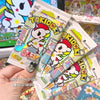 A hand holds several packs of Tokidoki collectible cards featuring a unicorn design.