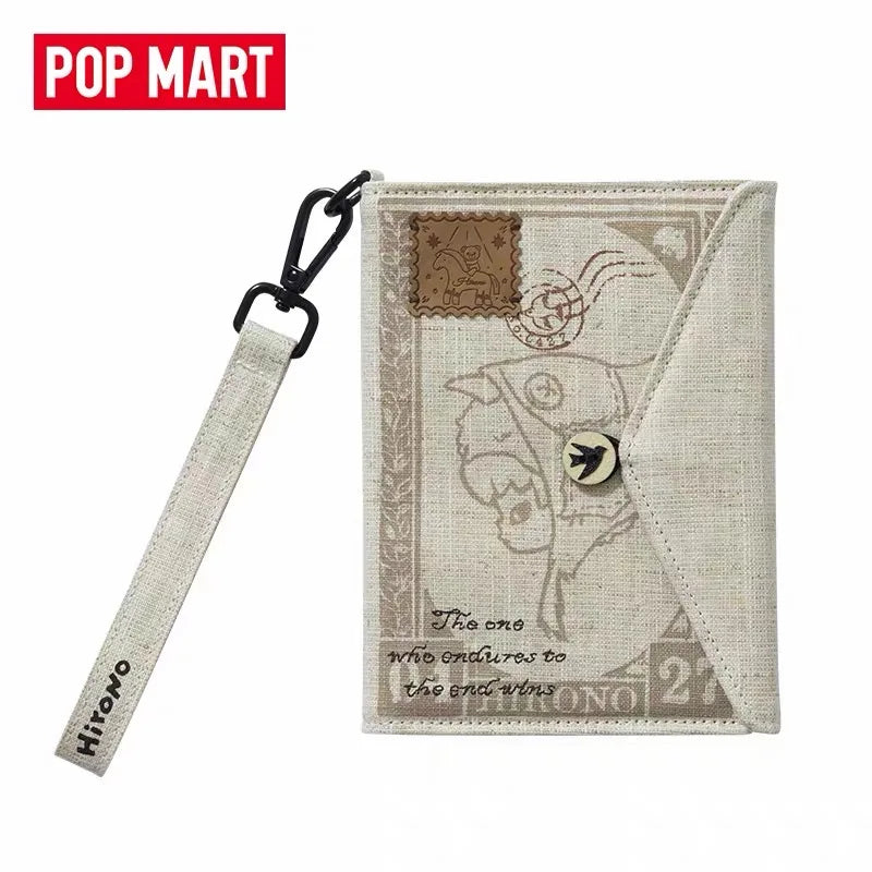 A POP MART Hirono Mist-Walker series blind box keychain featuring a beige fabric pouch with a decorative design.