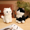 A white and black kitten plush toy sitting on a wooden surface.