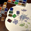 A collection of 20 metal watercolor paint colors arranged in a plastic palette on a light surface.