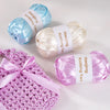 A set of three spools of various colored satin ribbon yarn for knitting and weaving displayed on a white surface.