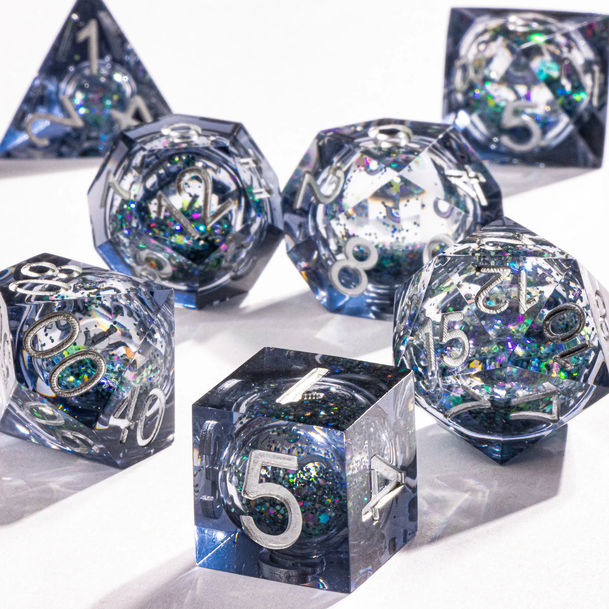 A collection of polyhedral dice with a galaxy finish scattered on a white surface.