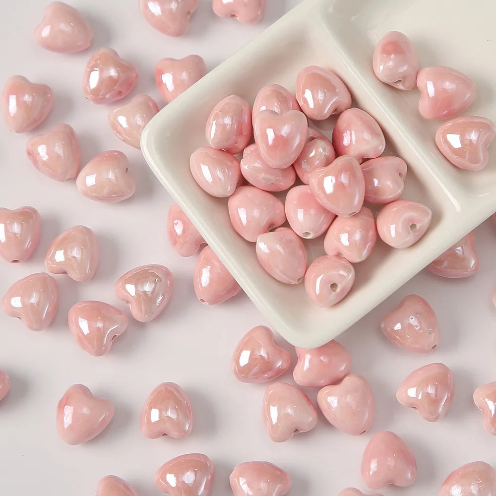 A pile of pink heart-shaped ceramic beads for jewelry making spread across a white tray.