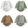 A collection of three embroidered cotton baby rompers in white, sage green, and beige.