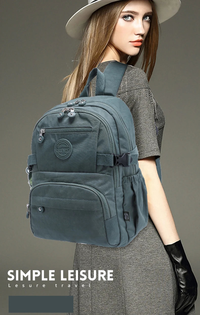 Une femme portant une robe grise tient un sac à dos de voyage gris et durable.