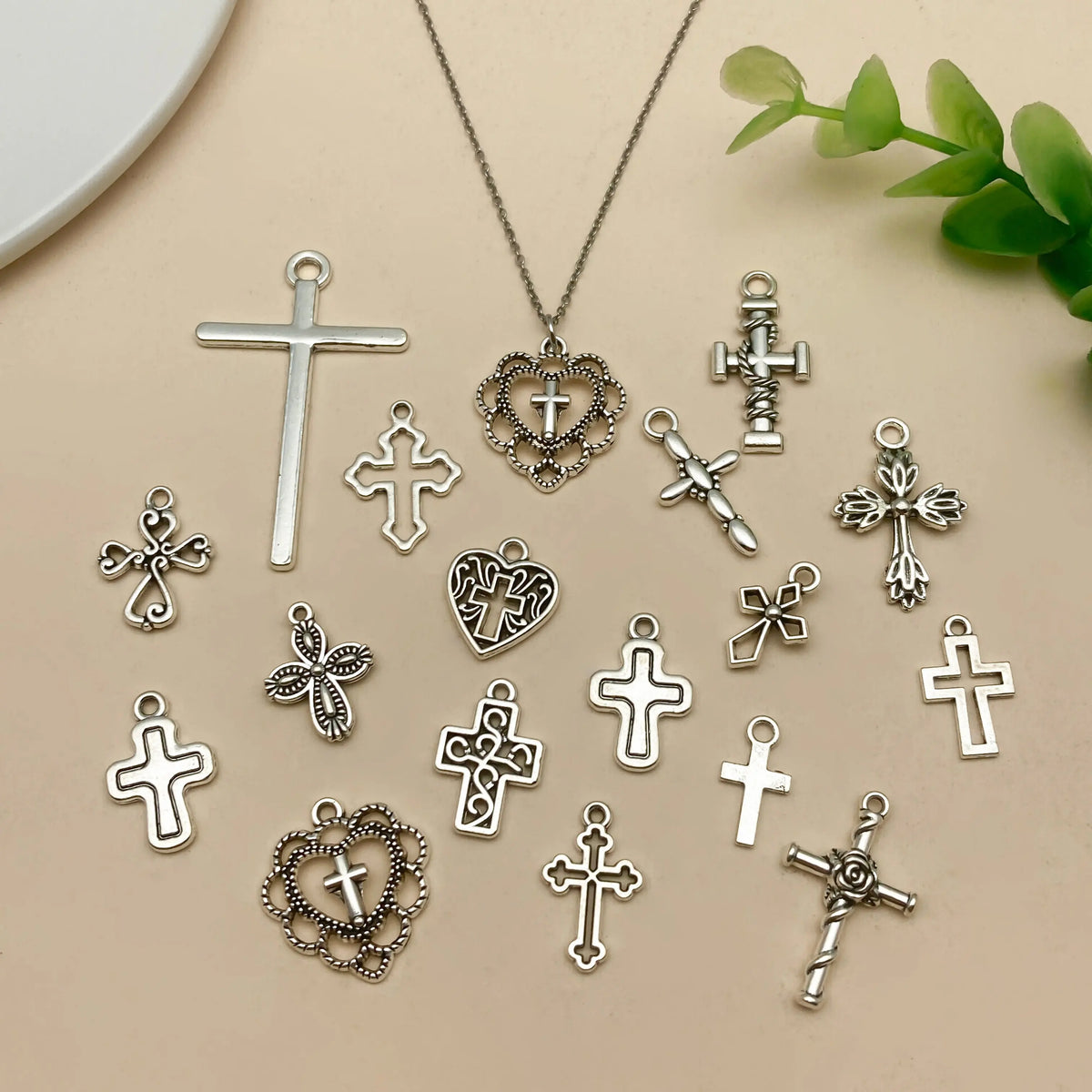 A collection of vintage silver cross charms and pendants scattered on a light beige surface.