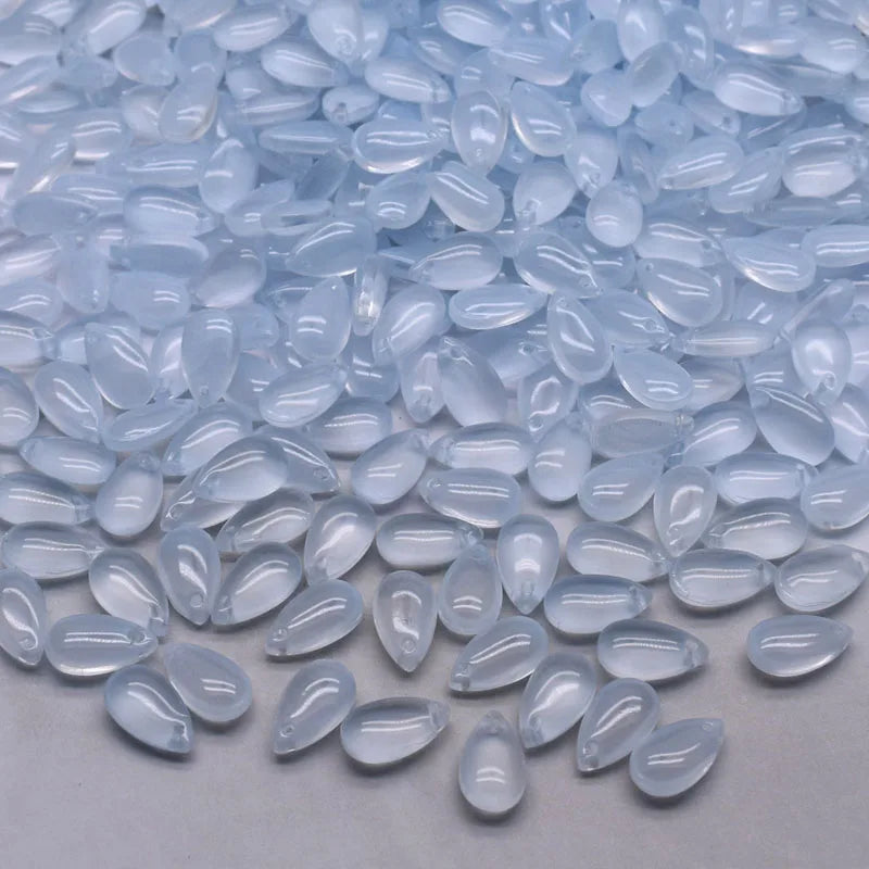 Clear, teardrop-shaped water drop glass beads scattered on a white surface for jewelry making