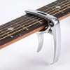 A silver metal guitar capo with a pick holder is shown clamped onto the fretboard of a wooden guitar neck.