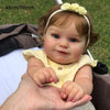 A close-up photo of a lifelike 48cm soft vinyl baby doll with 3D skin detail, wearing a yellow top and a flower headband.