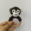 A crocheted monkey toy with white facial features and dark brown body, attached to a wooden ring.