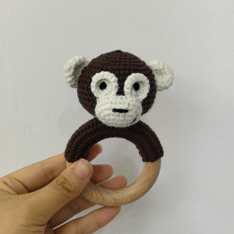 A crocheted monkey toy with white facial features and dark brown body, attached to a wooden ring.