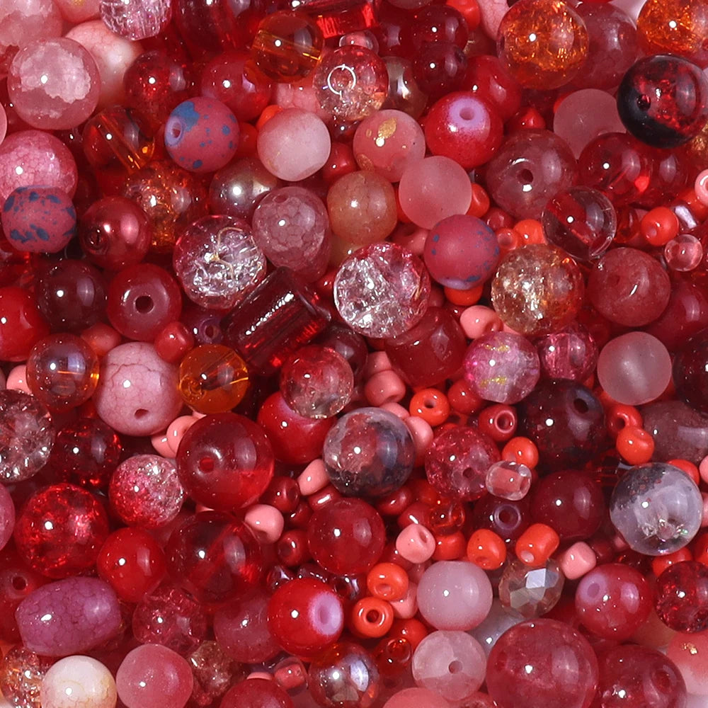 A close-up view of a vibrant mix of red, pink, and amber glass beads for DIY jewelry making