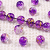 Purple gradient crystal glass beads with a golden crackle finish arranged in a line on a white textured surface