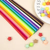 A colorful strip of paper with rainbow colors and small origami stars scattered on a light background.