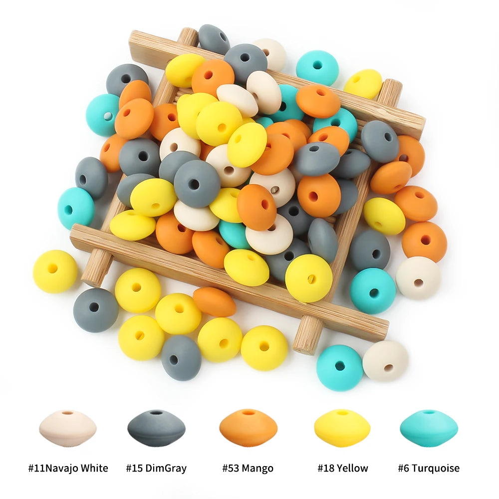A collection of silicone lentil beads in various colors including white, gray, orange, yellow, and turquoise arranged on a wo