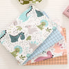 A stack of fabric featuring a dinosaur grid print in various colors like teal, green, and pink.