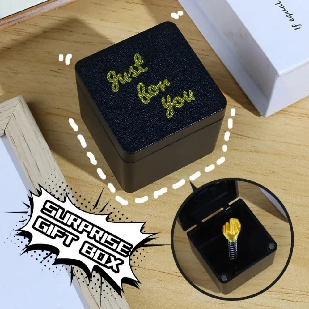 A black surprise gift box with gold text on top is shown next to a wooden surface and an open view of the inside.