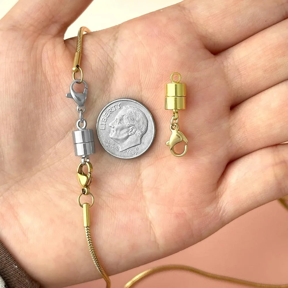 A hand displays magnetic jewelry clasps for necklaces and bracelets, including a silver and gold clasp attached to a coin.
