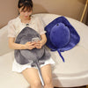 A woman is holding a gray plush toy shaped like a devil fish, resting on a white sofa.