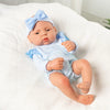 A lifelike vinyl reborn doll with a blue bow headband and matching outfit lying on white fabric.
