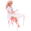 A blonde doll wearing a white dress is interacting with a white miniature table and medical accessories.